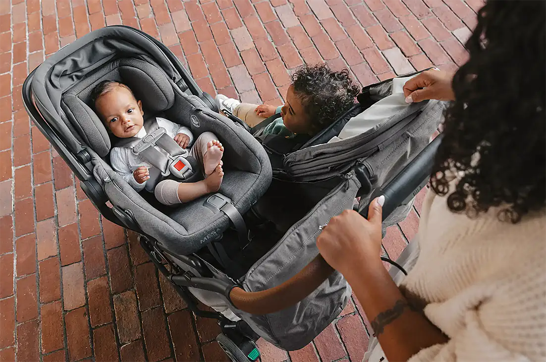 Infant secured in car seat installed on stroller with toddler in second seat